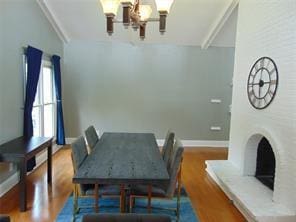 dining space with hardwood / wood-style floors, a large fireplace, vaulted ceiling, and a chandelier