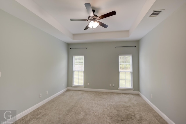 empty room with light carpet, ceiling fan, a raised ceiling, and a healthy amount of sunlight