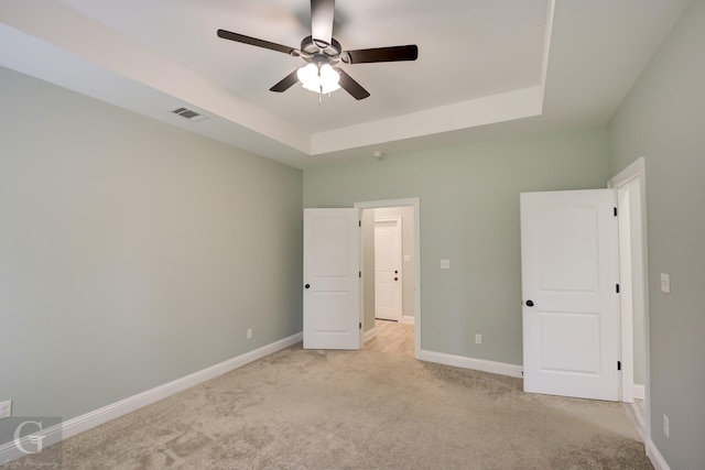 unfurnished bedroom featuring a raised ceiling, light carpet, and ceiling fan