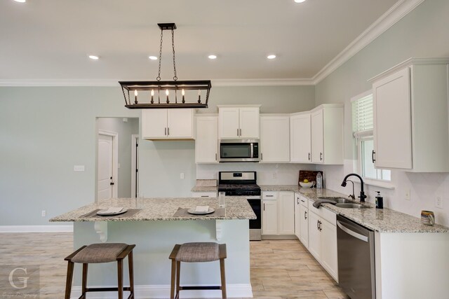 kitchen with white cabinets, sink, appliances with stainless steel finishes, a kitchen island, and light stone counters