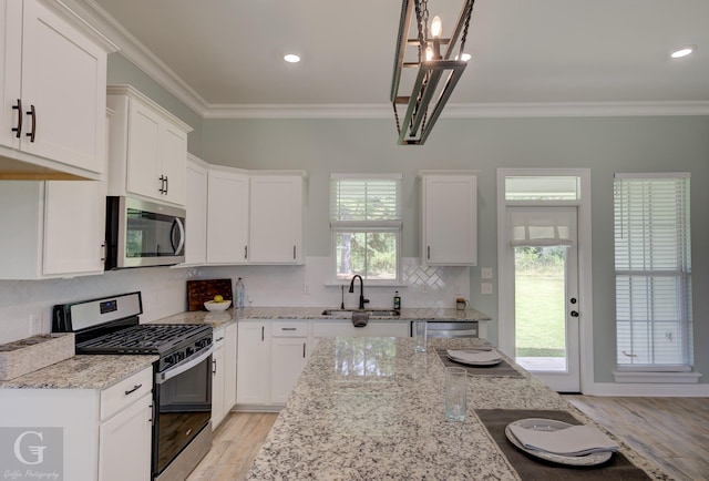 kitchen with sink, appliances with stainless steel finishes, white cabinetry, light stone counters, and ornamental molding