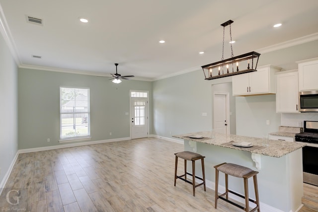 kitchen with a kitchen island, white cabinets, light hardwood / wood-style floors, stainless steel appliances, and light stone countertops