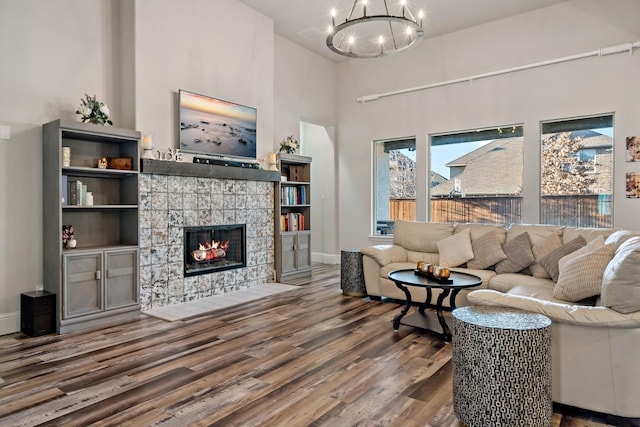 living room featuring hardwood / wood-style floors, a notable chandelier, a tile fireplace, and a towering ceiling