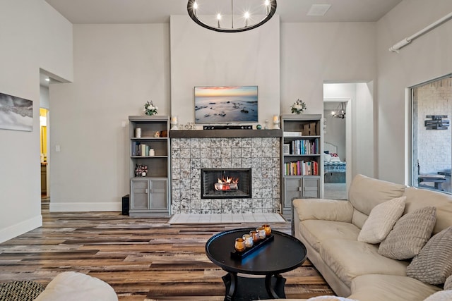 living room featuring wood-type flooring, a towering ceiling, a fireplace, and a chandelier