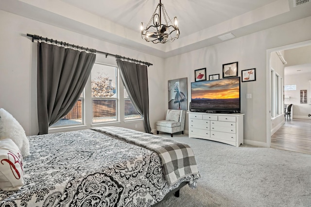 bedroom featuring light carpet, a tray ceiling, and an inviting chandelier