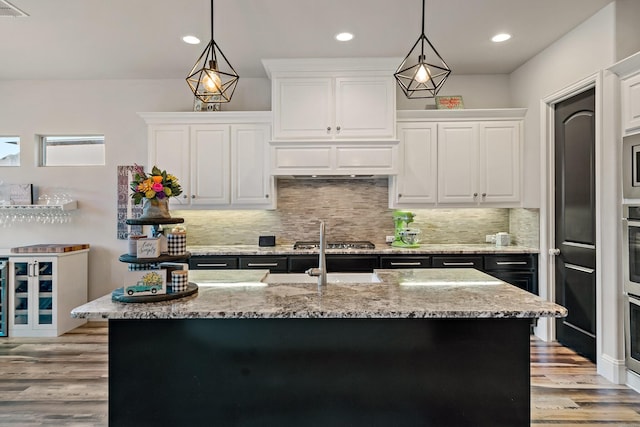 kitchen featuring white cabinets, decorative light fixtures, light stone counters, and an island with sink