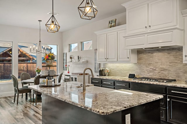 kitchen with white cabinets, hanging light fixtures, decorative backsplash, an island with sink, and stainless steel gas cooktop