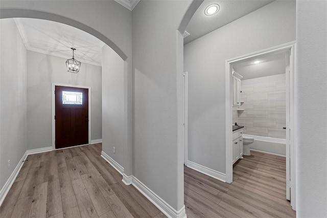 entryway with light hardwood / wood-style floors, crown molding, and a chandelier