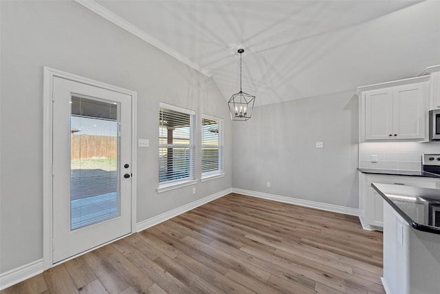 unfurnished dining area with light hardwood / wood-style floors, lofted ceiling, and a notable chandelier