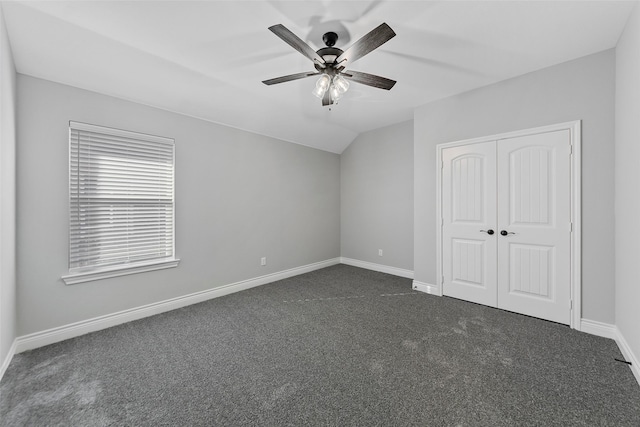 unfurnished bedroom with dark carpet, a closet, vaulted ceiling, and ceiling fan