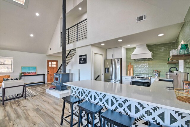 kitchen with custom range hood, tasteful backsplash, white cabinetry, kitchen peninsula, and stainless steel appliances