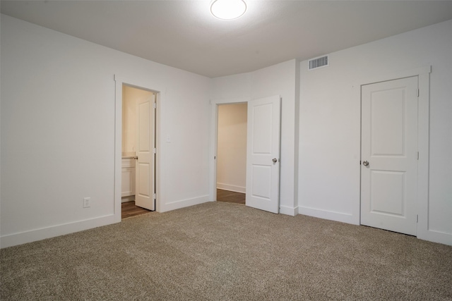 unfurnished bedroom with ensuite bathroom, a closet, and dark colored carpet