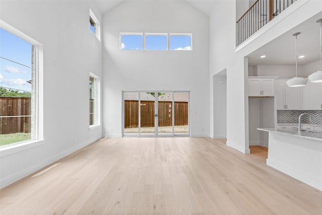 unfurnished living room featuring sink, plenty of natural light, a towering ceiling, and light hardwood / wood-style flooring