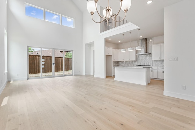 unfurnished living room with light hardwood / wood-style floors, a high ceiling, and an inviting chandelier