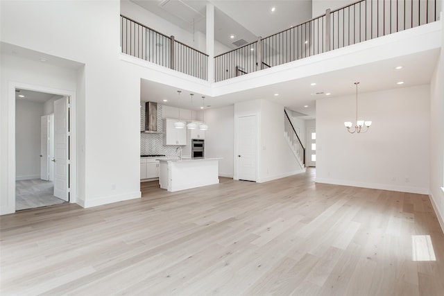 unfurnished living room featuring a towering ceiling, light hardwood / wood-style floors, an inviting chandelier, and sink