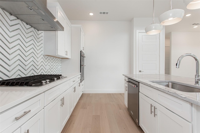 kitchen with pendant lighting, sink, wall chimney exhaust hood, appliances with stainless steel finishes, and white cabinetry