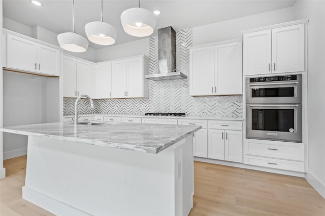 kitchen with sink, white cabinetry, hanging light fixtures, and wall chimney range hood