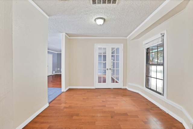 unfurnished room with a textured ceiling, light hardwood / wood-style flooring, crown molding, and french doors