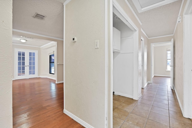 hall featuring french doors, light hardwood / wood-style floors, a textured ceiling, and ornamental molding