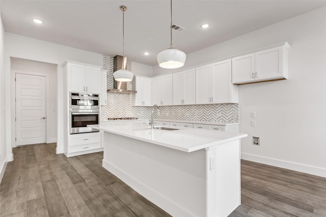 kitchen with double oven, sink, a kitchen island with sink, and white cabinets