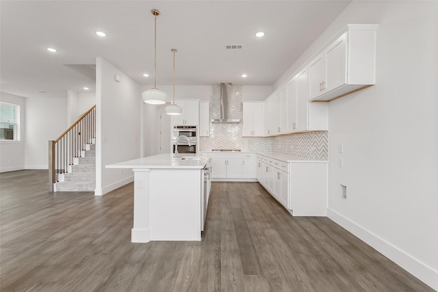 kitchen featuring wall chimney range hood, sink, gas stovetop, an island with sink, and white cabinets