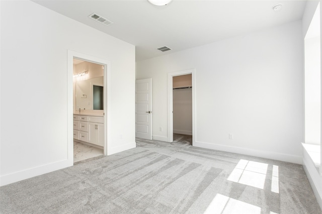 unfurnished bedroom with a walk in closet, ensuite bathroom, a closet, and light carpet