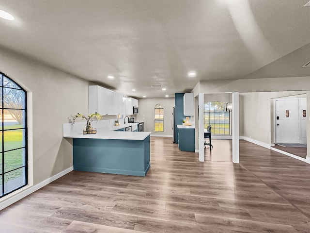 kitchen with kitchen peninsula, appliances with stainless steel finishes, light hardwood / wood-style floors, white cabinetry, and a chandelier