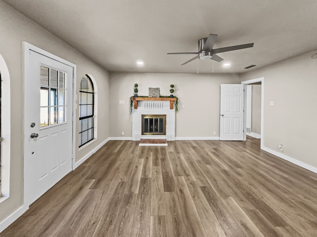 unfurnished living room with hardwood / wood-style flooring, ceiling fan, and a brick fireplace