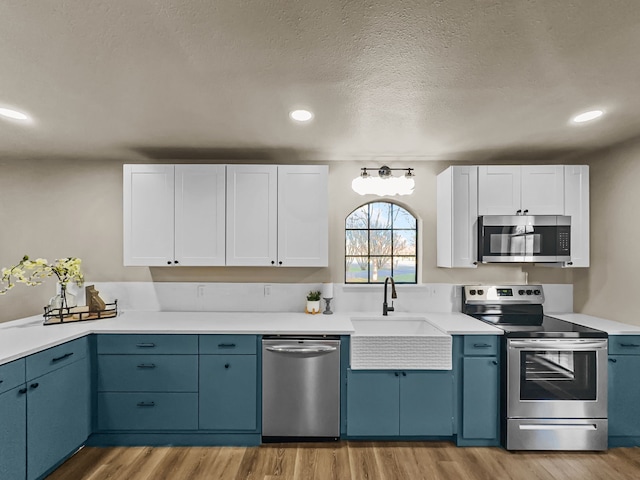 kitchen with appliances with stainless steel finishes, a textured ceiling, blue cabinets, sink, and white cabinetry