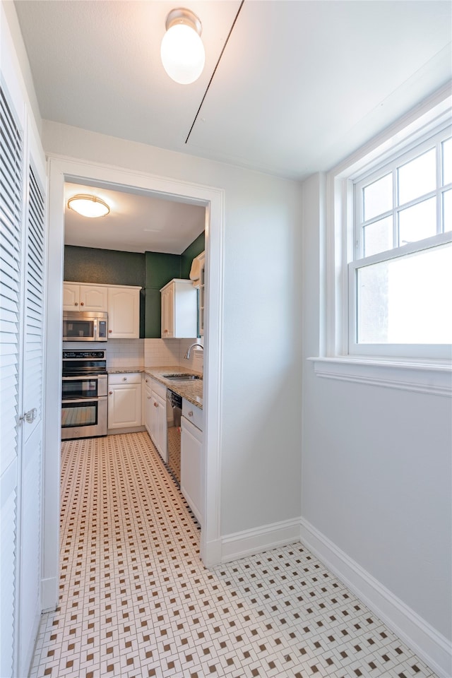 kitchen featuring a sink, tasteful backsplash, white cabinetry, stainless steel appliances, and baseboards