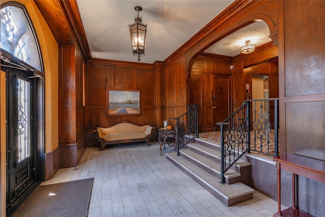 entrance foyer featuring wooden walls, a chandelier, stairs, ornamental molding, and arched walkways