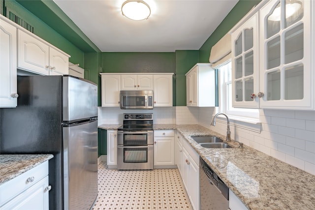 kitchen with glass insert cabinets, decorative backsplash, appliances with stainless steel finishes, white cabinets, and a sink