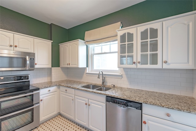 kitchen with tasteful backsplash, glass insert cabinets, appliances with stainless steel finishes, white cabinets, and a sink