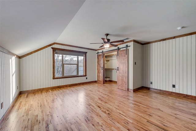 bonus room featuring ceiling fan, lofted ceiling, a barn door, and light wood-type flooring