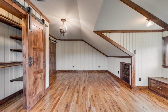 additional living space featuring lofted ceiling, a barn door, a chandelier, and light hardwood / wood-style flooring