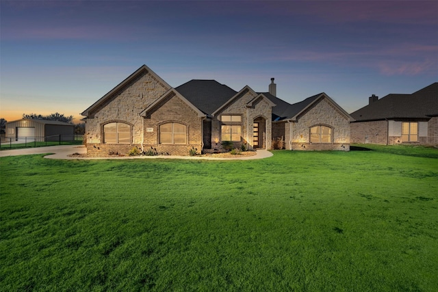 french country home with a front yard, brick siding, fence, and a chimney