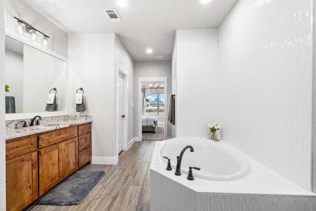 bathroom featuring wood-type flooring, vanity, and a relaxing tiled tub