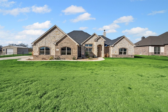 french country inspired facade with brick siding, a chimney, fence, and a front yard