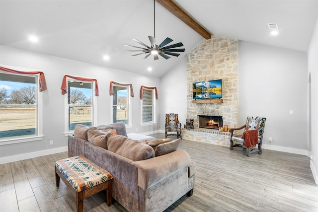 living room featuring vaulted ceiling with beams, ceiling fan, a stone fireplace, and light wood-type flooring