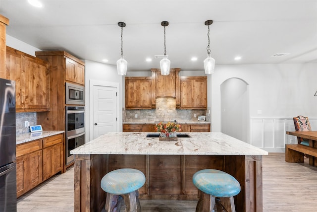 kitchen featuring light stone countertops, a large island with sink, decorative light fixtures, and appliances with stainless steel finishes