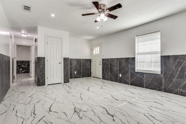 spare room with ceiling fan and tile walls