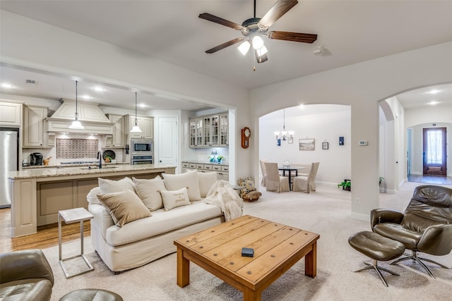 living room featuring sink, ceiling fan with notable chandelier, and light carpet