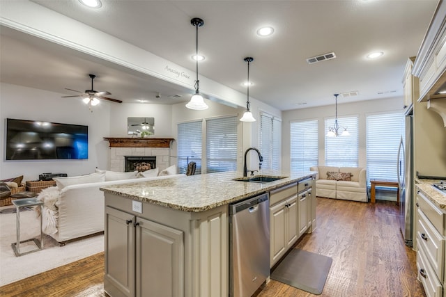 kitchen with sink, hanging light fixtures, a kitchen island with sink, stainless steel appliances, and light stone countertops