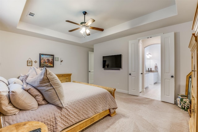 bedroom with light carpet, a tray ceiling, and ensuite bathroom