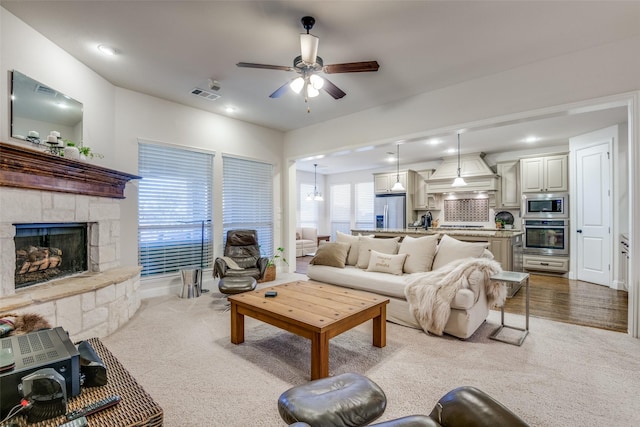 living room featuring light carpet, a fireplace, and ceiling fan