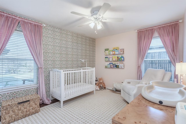 bedroom with ceiling fan, multiple windows, and a nursery area