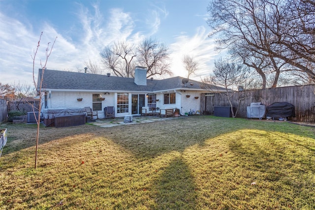 back of house featuring a lawn, a patio, and a hot tub