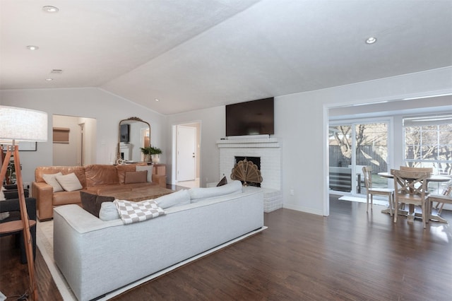 living room with vaulted ceiling, a brick fireplace, and dark wood-type flooring