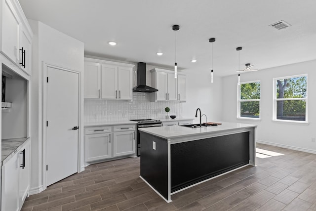 kitchen with white cabinetry, stainless steel electric range oven, wall chimney exhaust hood, and an island with sink