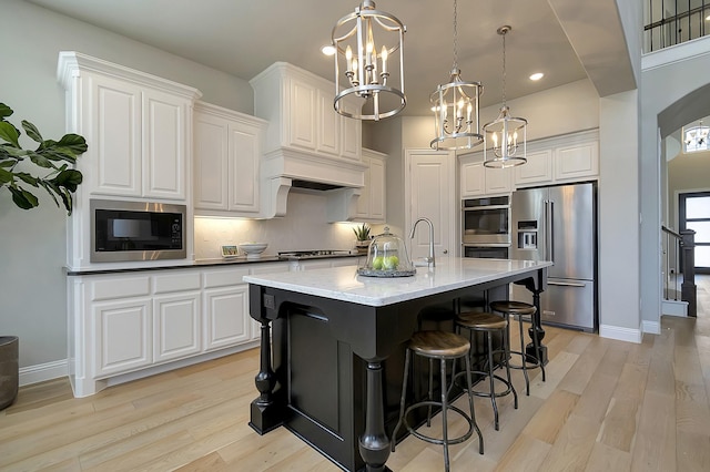 kitchen with stainless steel appliances, a center island with sink, white cabinets, and hanging light fixtures